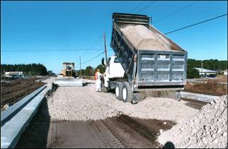 a dump truck spreading gravel for a road with a bulldozer coming in the opposite lane to level the gravel
